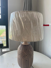 Table lamp with a patterned base and beige shade on a surface.