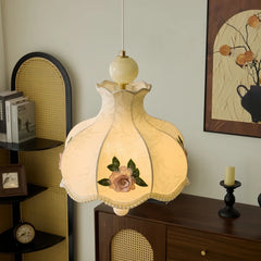 Champagne fabric pendant light with floral rose embroidery and beaded trim hanging in a room with wooden furniture.