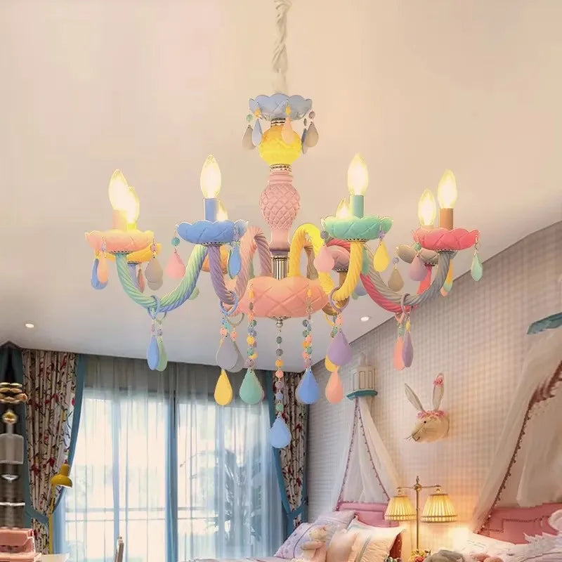 A colorful macaron crystal chandelier with floral elements and hanging teardrop crystals, shown in a bedroom with pink bedding.