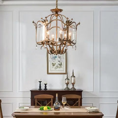 A gold candelabra pendant light with a glass shade and crystal droplets, showcased above a dining table setting.