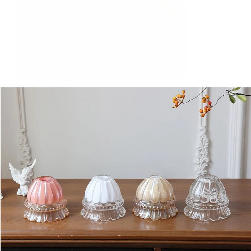 Four decorative glass lampshades on a wooden surface with a white wall and decorative branch in the background.