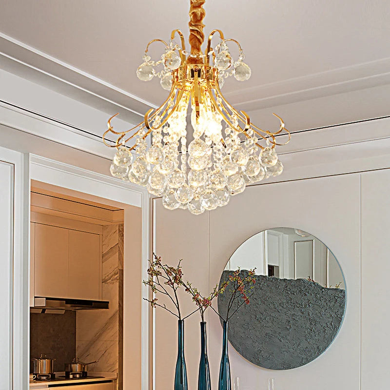 A gold-toned crystal chandelier with clear crystals, mounted on a white ceiling.
