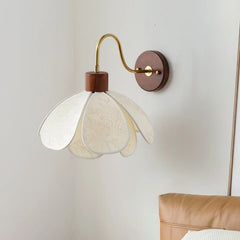 Wall-mounted lamp with white floral shade and wooden base on a light gray wall.