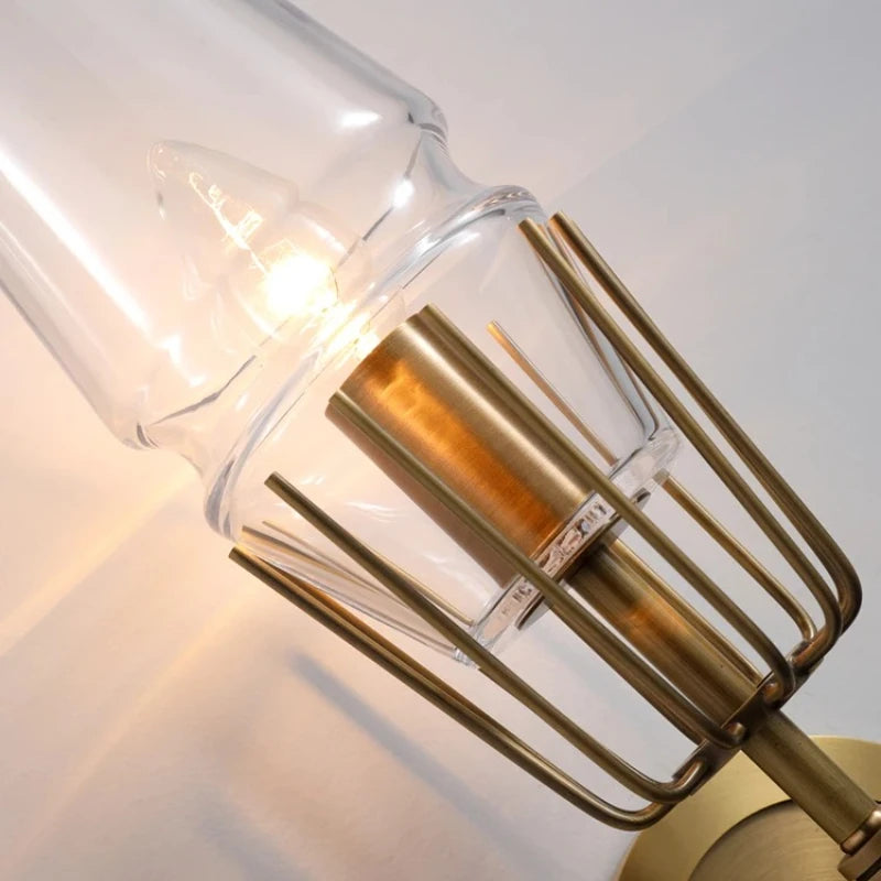 Gold wall sconce with clear glass shade on a neutral background