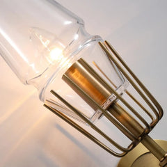 Gold wall sconce with clear glass shade on a neutral background