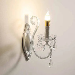 White crystal candelabra style wall sconce illuminated against a white wall.
