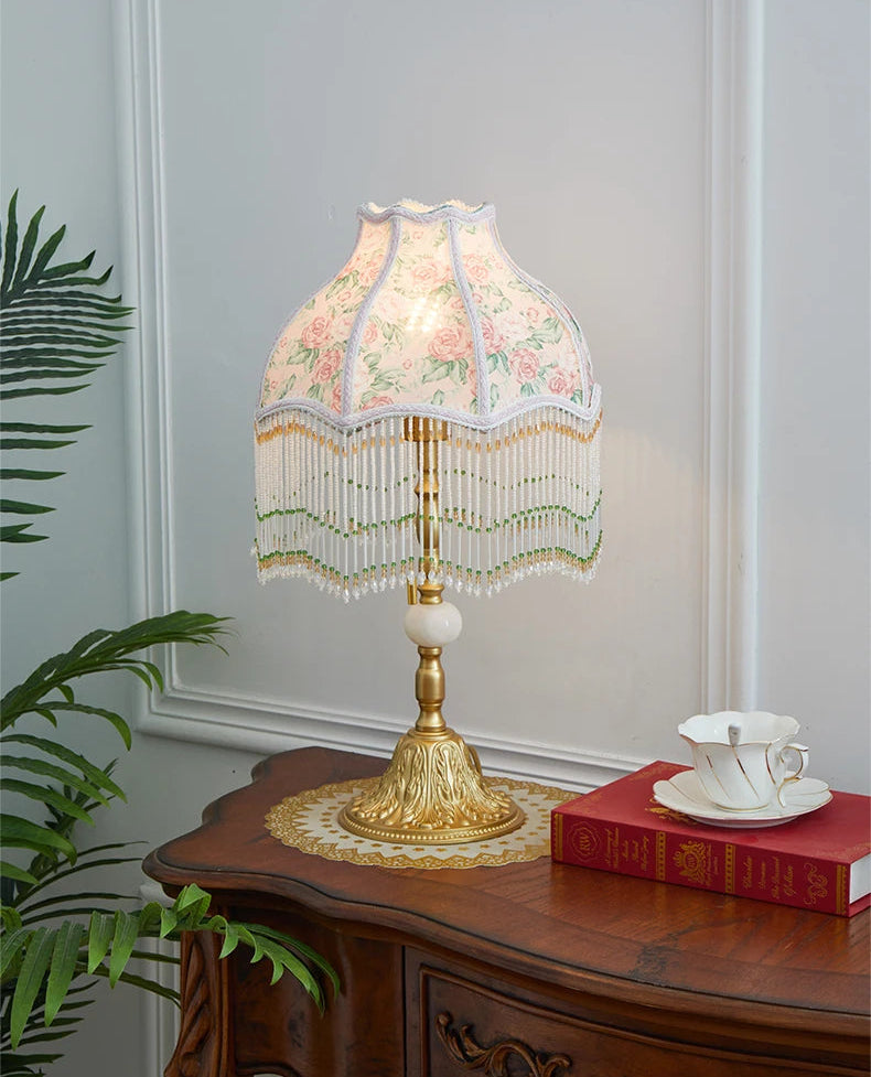 Decorative table lamp with floral lampshade on a wooden table next to a plant.