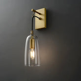 A modern gold and clear glass bell wall sconce mounted on a dark gray wall, with the light on.