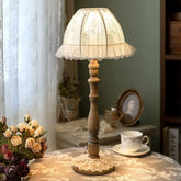 A vintage-style wooden table lamp with a ruffled, lace-trimmed fabric shade, casting a warm glow.