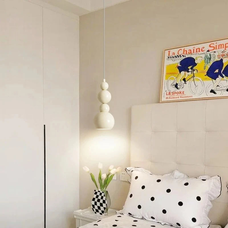 Cream gourd-shaped pendant light hanging over a bed with a framed bicycle print on the wall.