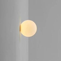 A white frosted glass sphere wall sconce mounted on a light gray corner wall, emitting a soft warm light.