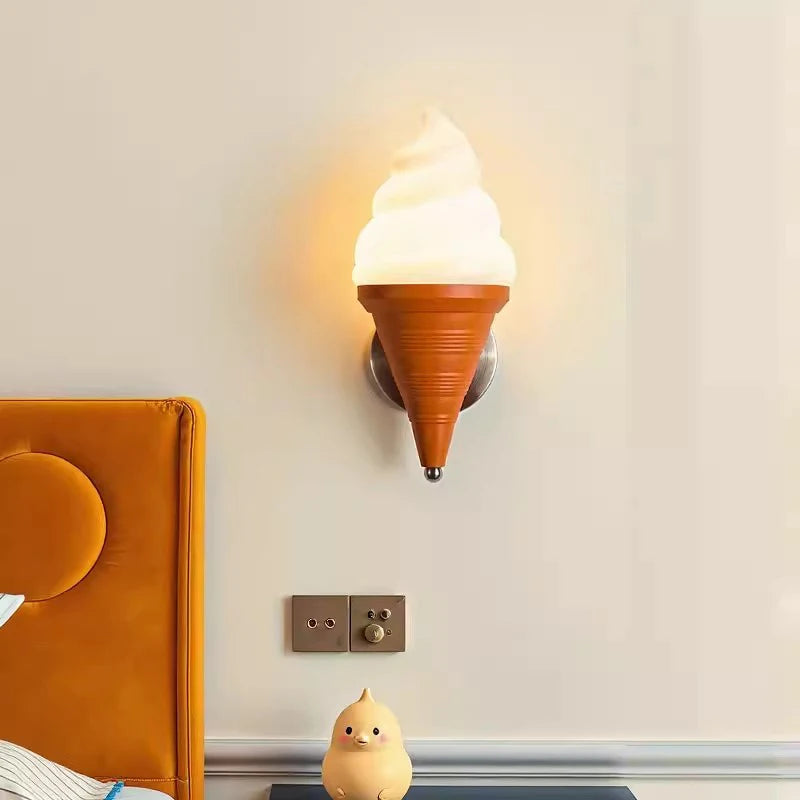 An ice cream cone wall sconce illuminated in a bedroom setting near a bed and a small decorative chick figurine.