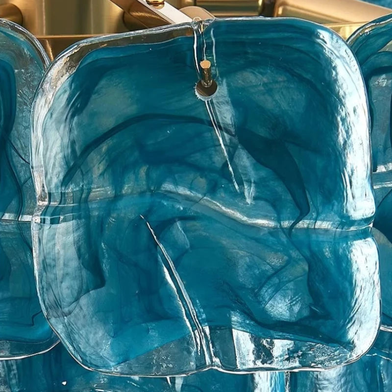 Close-up view of a textured blue glass panel from the chandelier, showing swirls of color and a hole for suspension.