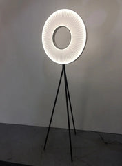 Modern floor lamp with a circular design on a tripod base against a plain background