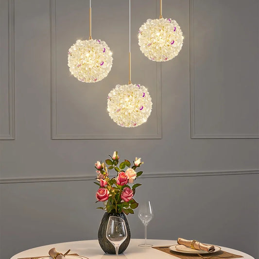 Three gold crystal orb pendant lights hanging over a dining table with a vase of roses.