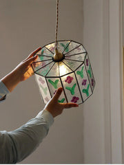 Hand holding a stained glass lamp with floral designs against a neutral background