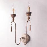 Distressed gold metal wall sconce with two candle-style light holders and decorative wooden beads hanging from curved arms against a white wall.
