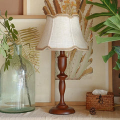 Wooden table lamp with a white lampshade on a surface with decorative elements.