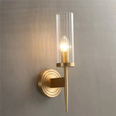 Gold wall sconce with clear glass shade on a gray wall