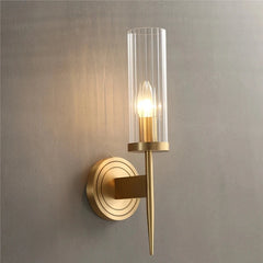 Gold wall sconce with clear glass shade on a gray wall