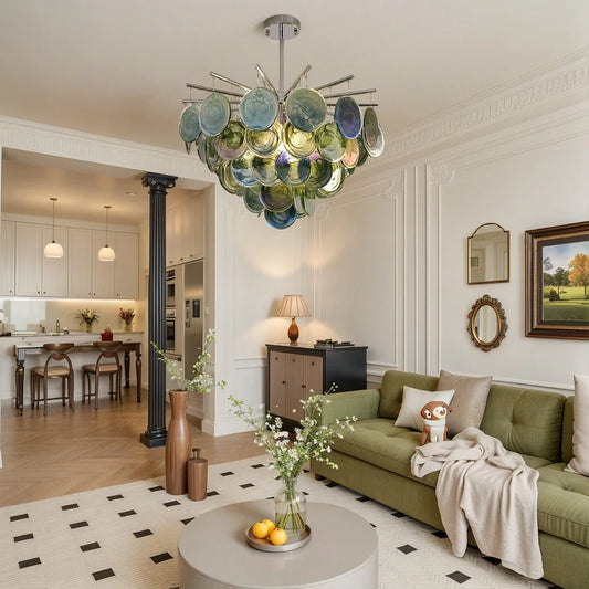 A modern chandelier with layered green and blue glass discs hanging from a chrome frame, illuminating a contemporary living room.