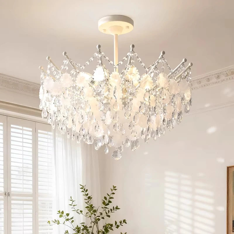 The gold crystal chandelier illuminated in a room setting, casting light patterns on the ceiling and walls.