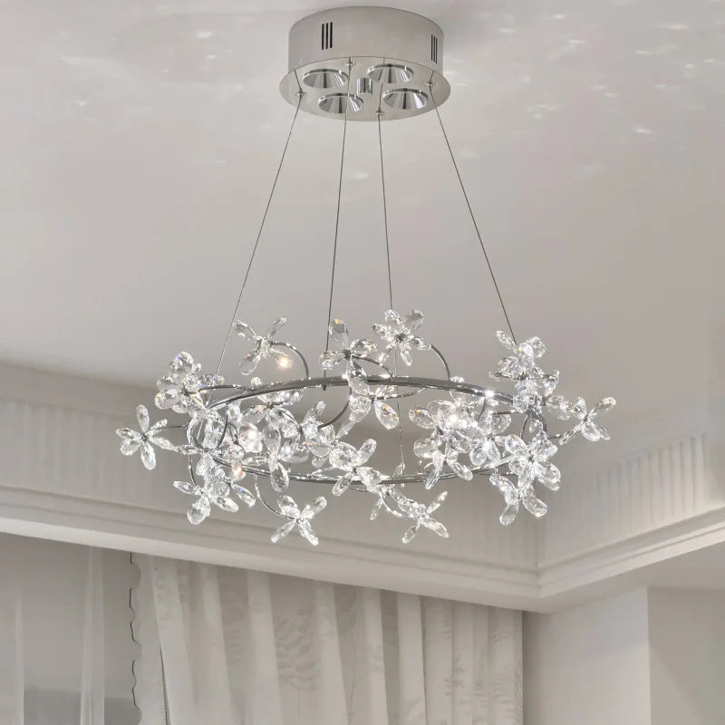 A detailed view of a chrome ring chandelier featuring numerous clear crystal floral accents, illuminated and casting light patterns.