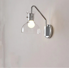 Close-up of a polished chrome wall sconce with a clear glass dome shade and a metal arm against a white background.
