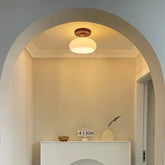 Frosted glass dome ceiling light with a wood base, mounted in an arched entryway.