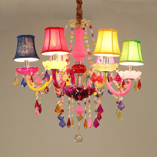 A vibrant and colorful chandelier with multiple fabric shades in red, blue, yellow, and green, adorned with numerous hanging crystals of various shapes and colors, suspended from a central pink and red ornate fixture.