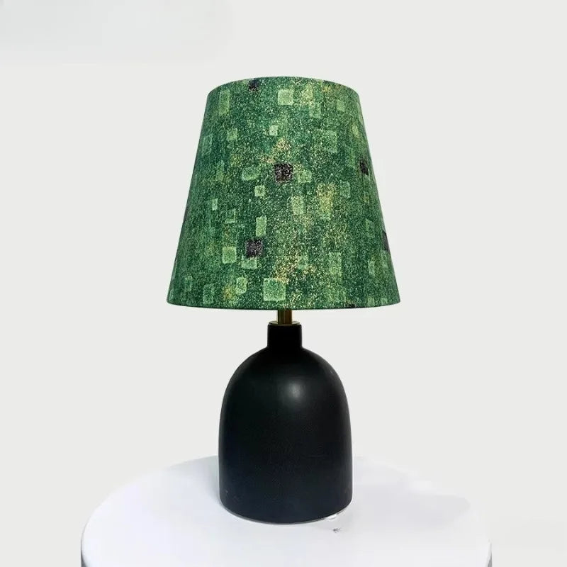 Black ceramic table lamp with a textured green fabric shade featuring a subtle geometric pattern, on a white surface.