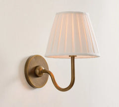 Wall-mounted lamp with a white pleated shade and brass arm on a light gray background