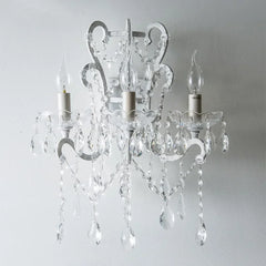 Crystal chandelier with three candle-style lights on a plain background