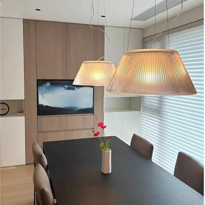 Two clear pleated glass drum pendant lights hanging above a dining table.