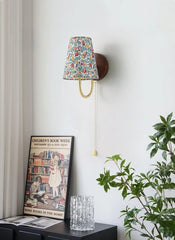 Wall-mounted lamp with floral shade in a room with a book, glass, and plant.