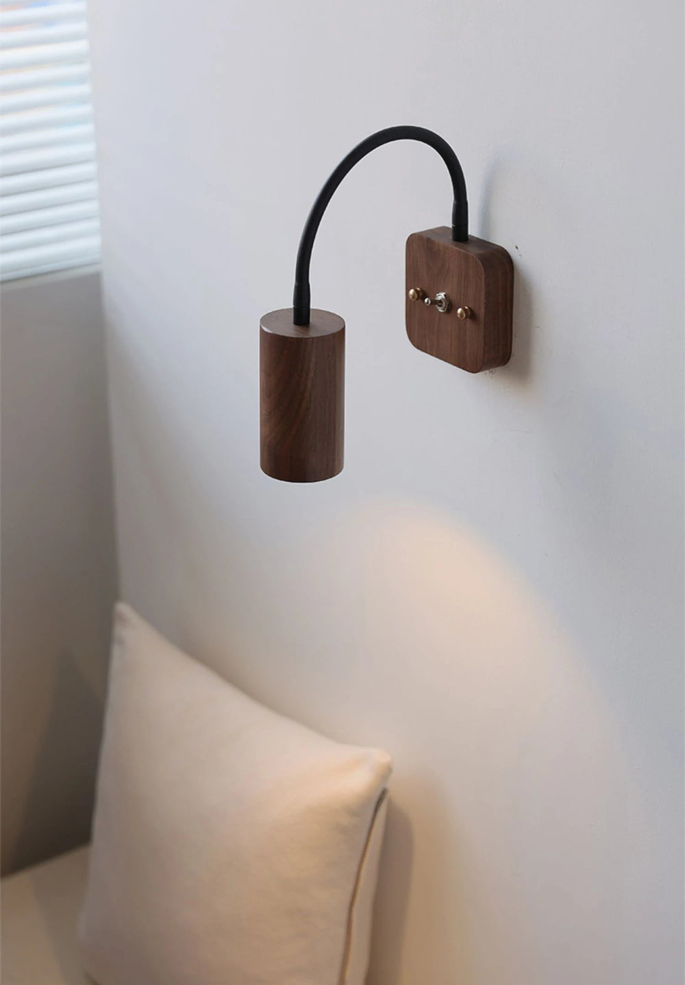 Wooden wall lamp with flexible arm on a white wall near a window.