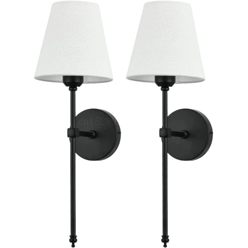 Two matte black wall sconces with white fabric shades against a white background.