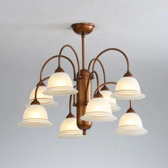 A view of a brushed gold chandelier with eight frosted glass bell-shaped shades, illuminated and casting a warm glow, against a subtly textured ceiling.