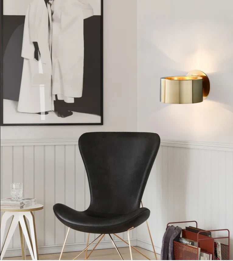 Modern interior with a black chair, gold wall sconce, and abstract art on a white wall.