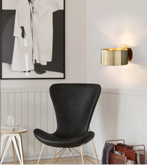 Modern interior with a black chair, gold wall sconce, and abstract art on a white wall.