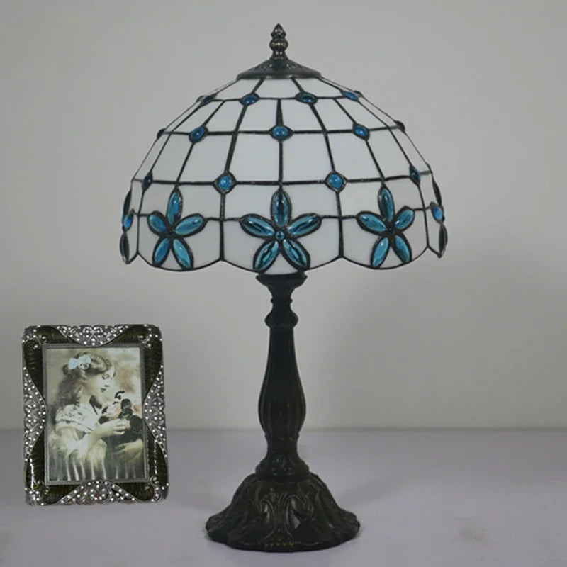 Blue Tiffany stained glass floral table lamp with a dark base, shown with a framed photo.
