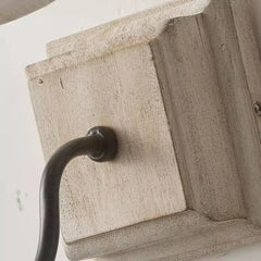 Close-up view of the distressed white wood backplate of a wall sconce, showing texture and the point where a dark metal arm attaches.