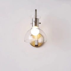Front view of a brushed nickel wall sconce with a clear glass dome shade and an integrated light bulb, mounted on a white wall.