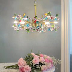 A gold chandelier with colorful crystal flowers, shown above a bouquet of pink roses.