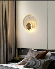 Modern wall lamp above a bed with decorative pillows in a bedroom setting.