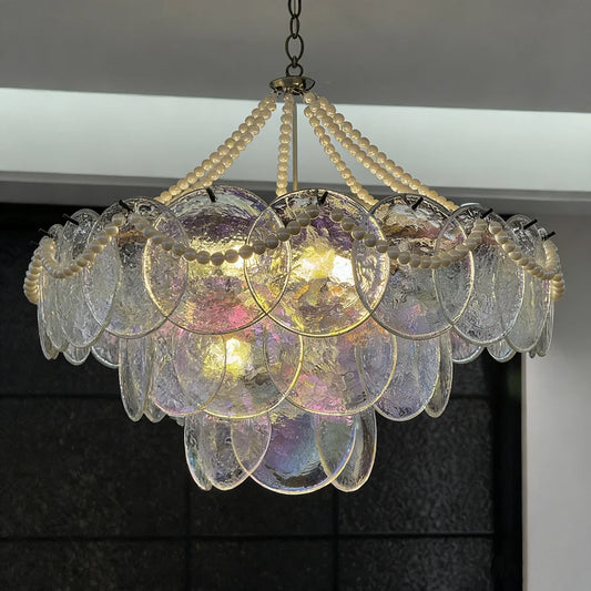 Close-up of a tiered glass chandelier with pearl bead strands and iridescent glass discs illuminated by warm light.