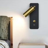 Close-up of a black wall sconce with a gold adjustable spotlight head and integrated USB port mounted on a white wall.