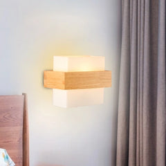 A wood and glass LED wall sconce installed on a wall next to a wooden bed frame and grey curtains.