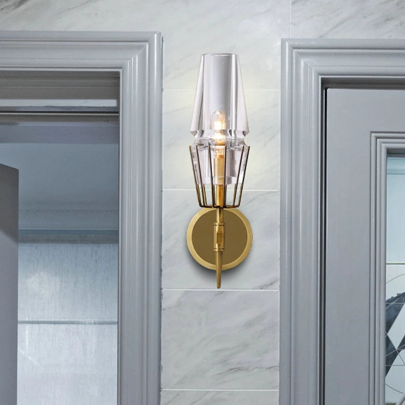 Single clear glass crystal wall sconce with brushed gold frame installed between two doorways with marble tile.