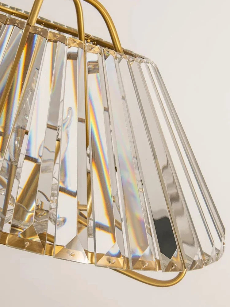 A gold crystal faceted pendant light with a wide, flared shade, showcasing prismatic light effects.